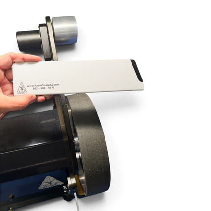Razor Sharp AZ white rigid ABS knife edge guard held in hand against a sharpening machine