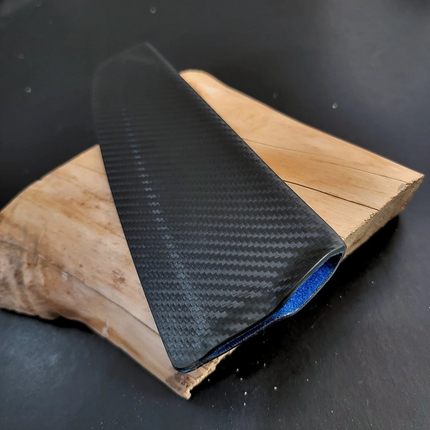Razor Sharp AZ black carbon fiber knife sheath with blue interior lining resting on a piece of natural wood