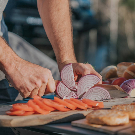 Razor Sharp AZ Overland Chef 8-inch camp knife slicing a red onion on a wooden cutting board outdoors.
