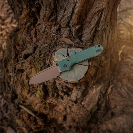 Raccoon 2.0 Top Liner Lock folding knife with 3.25" copper-dune blade and green Micarta handle on a tree stump.