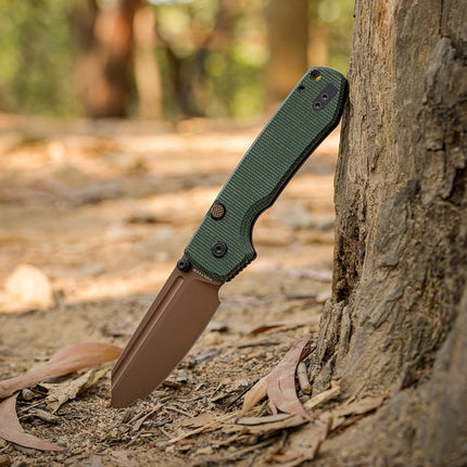 Raccoon 2.0 A2907 drop-point knife with copper-dune blade and green Micarta handle leaning against a tree.