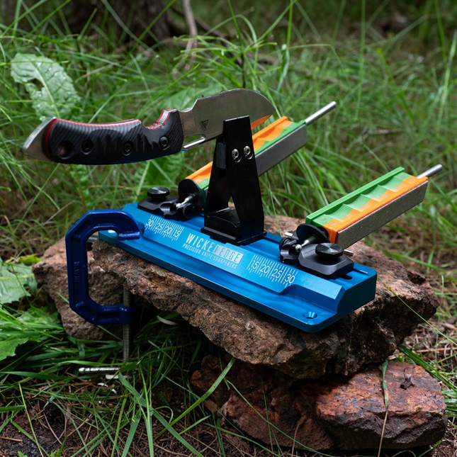 Razor Sharp AZ Wicked Edge GO WE60 portable knife sharpener with blue anodized base and diamond stones on a rock