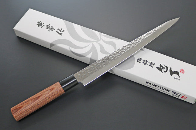 KC-959 Sujihiki Carbon 240mm Kanetsune knife with hammered blade and wooden handle beside its packaging box.