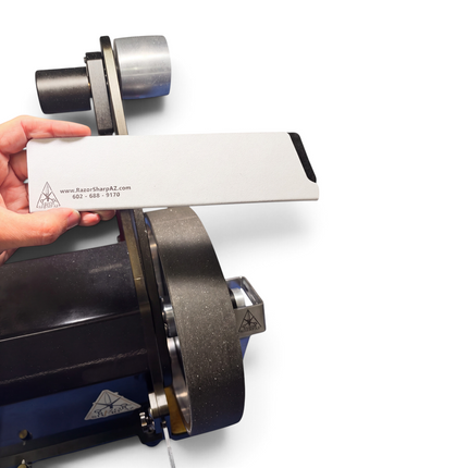 Razor Sharp AZ white velvet-lined knife edge guard held in hand near a belt grinder for kitchen knife storage
