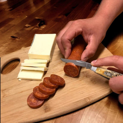 Razor Sharp AZ Case 6.5 BoneStag Mini Trapper folding knife slicing sausage on a wooden cutting board with cheese