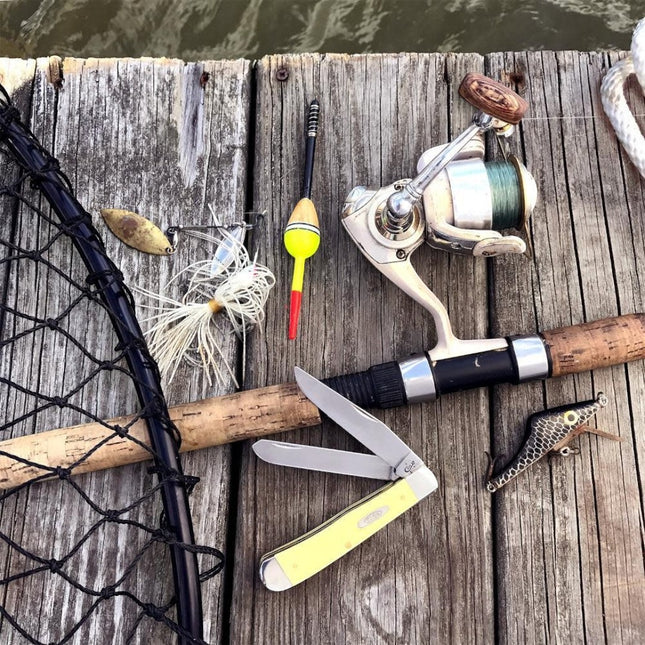 Razor Sharp AZ Case Yellow Synthetic Trapper knife with dual carbon steel blades resting on a wooden fishing dock.