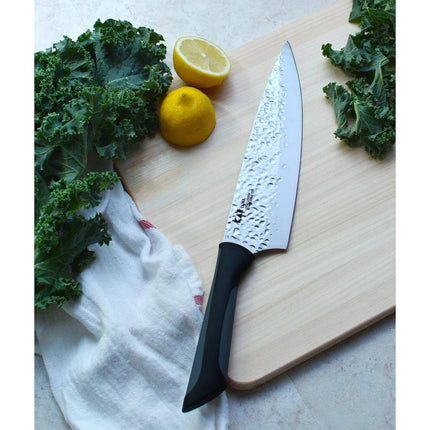 Razor Sharp AZ Kai Luna 8" chef's knife with hammered stainless steel blade and black handle, next to lemons and kale.