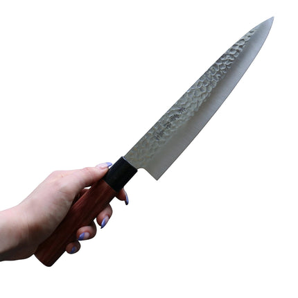 Razor Sharp AZ Kanetsune Gyuto chef knife with a hammered Tsuchime finish and wood handle held by a hand.