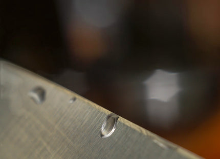 Close-up of a wet, brushed metal knife blade edge, highlighting water droplets and the sharp bevel. Razor Sharp AZ.