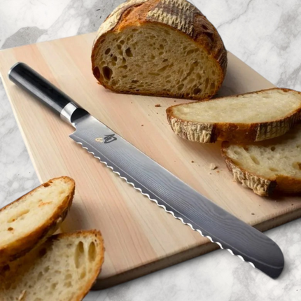 Razor Sharp AZ Shun Classic 9-inch serrated bread knife with Damascus steel blade and ebony PakkaWood handle on board
