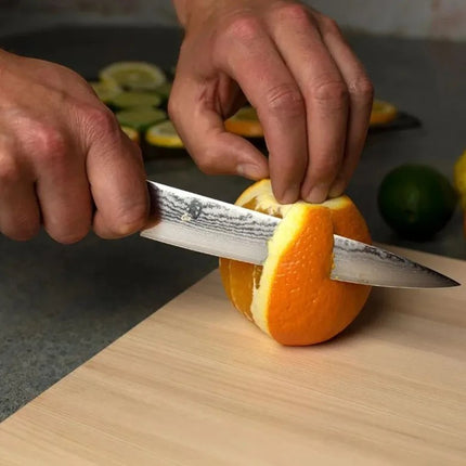 Razor Sharp AZ Shun Classic 6-inch utility knife with Damascus steel blade slicing a fresh orange on a wooden board