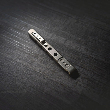 Razor Sharp AZ Ti-Pry titanium pocket pry bar with integrated clip and machined holes on a dark textured surface