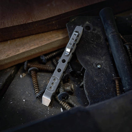 Razor Sharp AZ Ti-Pry titanium pocket pry bar with integrated clip resting on a pile of screws and hardware