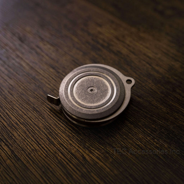 Razor Sharp AZ TEC Accessories Ti-Tape titanium tape measure with a stonewashed finish on a dark wooden surface